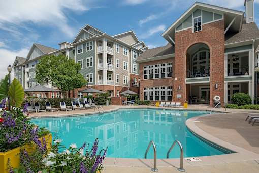 A large swimming pool is surrounded by a yellow planter box with purple and white flowers.