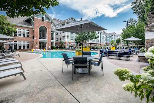 A pool area with chairs and umbrellas in front of a building.