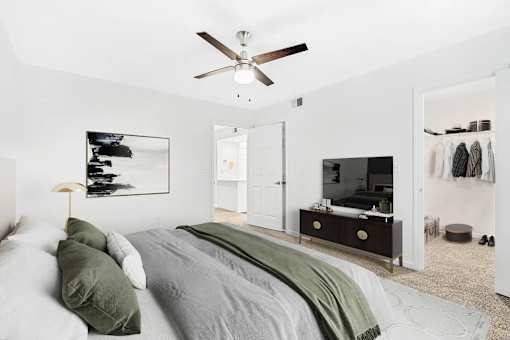 A bedroom with a bed, a ceiling fan, and a closet with clothes hanging.