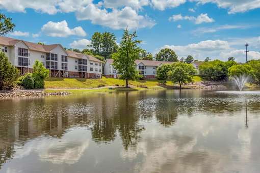 A serene lake in front of apartment buildings under a clear blue sky.