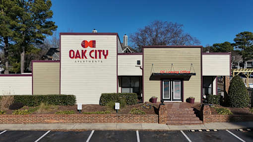 The front of the Oak City Apartments building is shown with a clear blue sky in the background.