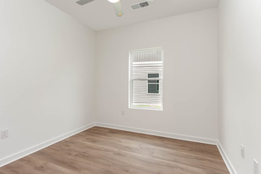 a room with white walls and a window and wood floors
