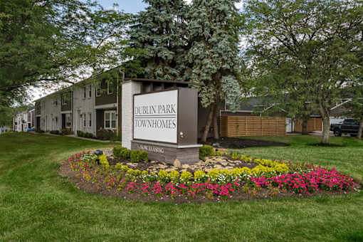 A sign for Dublin Park Townhomes is surrounded by flowers and greenery.