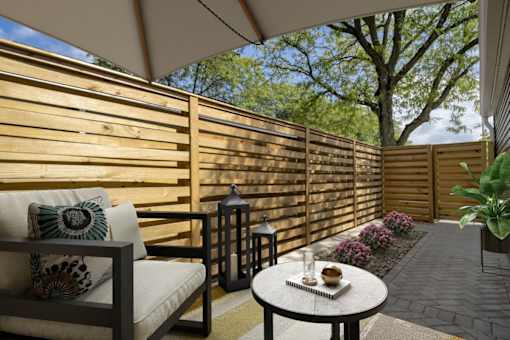 A patio with a white couch and a table with a vase on it.