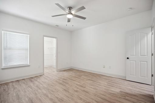 A room with a ceiling fan and light, hardwood floors, and white walls.
