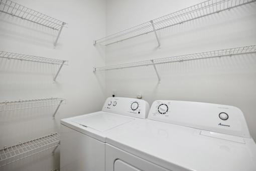 A white washing machine in a laundry room with shelves above it.