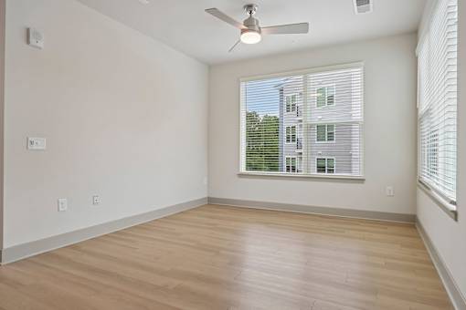 A room with a ceiling fan and a window showing a building outside.