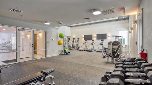 A gym with a variety of equipment including dumbbells, a bench, and a treadmill.