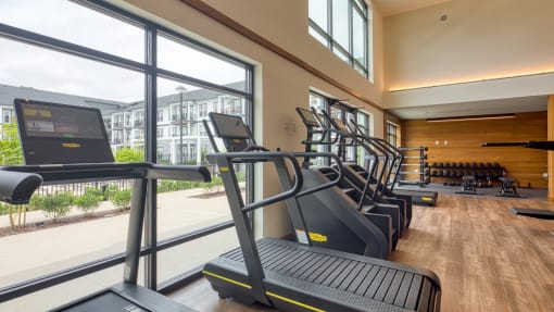 a gym with cardio equipment and large windows at the district at highland village apartments at Ainsworth, Richmond