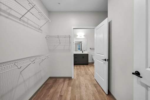 A white walk in closet with a door open to a hallway.