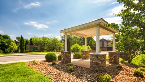 a covered porch with stone pillars on the side of a road