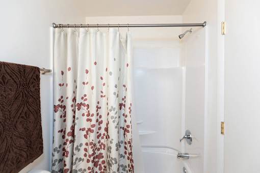 A white shower curtain with red and grey flowers is hanging in a white bathroom.