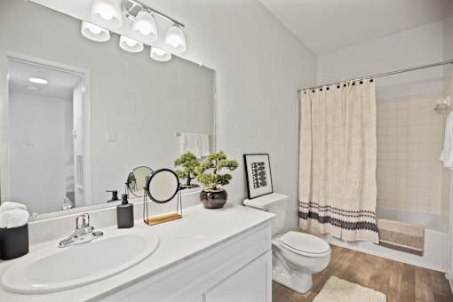 A bathroom with a white sink, toilet, and a mirror with lights above it.
