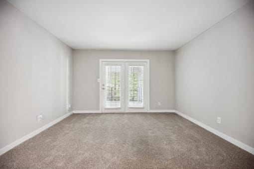 an empty living room with white walls and a door to a balcony