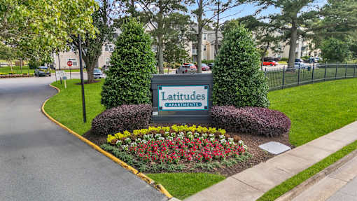 A sign for Latitudes Capayment surrounded by greenery and flowers.