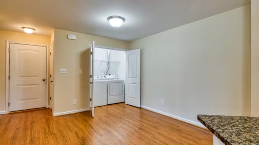 an empty living room with wood flooring and a kitchen with white appliances