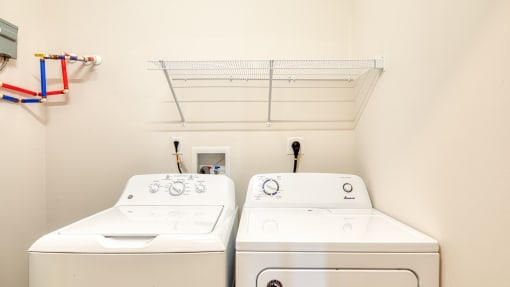 two washers and a dryer in a laundry room with a shelf above them