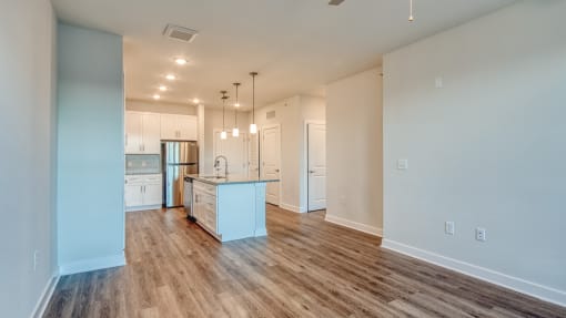 an empty living room with a kitchen with a sink and refrigerator at The Bella at Westchester, Midlothian, VA