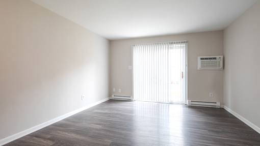 A spacious room with wooden flooring and a sliding glass door.