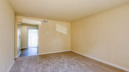 A large empty room with a carpeted floor and a doorway leading to another room.