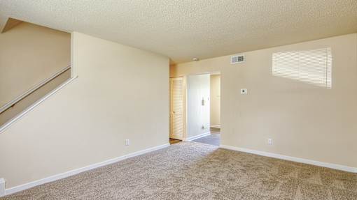 A room with a carpeted floor and a staircase leading to another room.