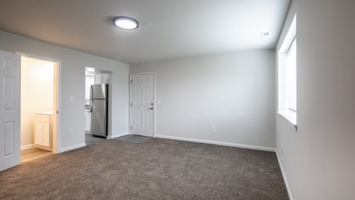 an empty living room with white walls and a door to the kitchen