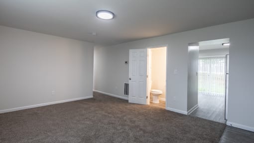 an empty living room with a door to a bathroom and a toilet