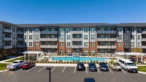 A large apartment complex with a pool and cars parked in the lot.
