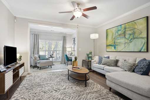 A living room with a grey couch, a coffee table, a television, and a painting on the wall.