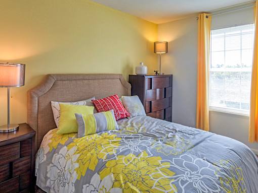 A bed with a grey and yellow comforter with a headboard and a nightstand with a lamp.