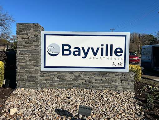 A property sign for Bayville Apartments is displayed in front of a stone wall.