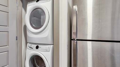 A white washing machine is stacked on top of another white washing machine in a kitchen.