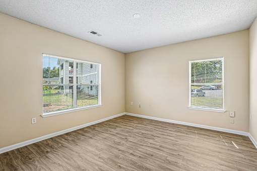 A room with light brown walls and wooden flooring with two windows.