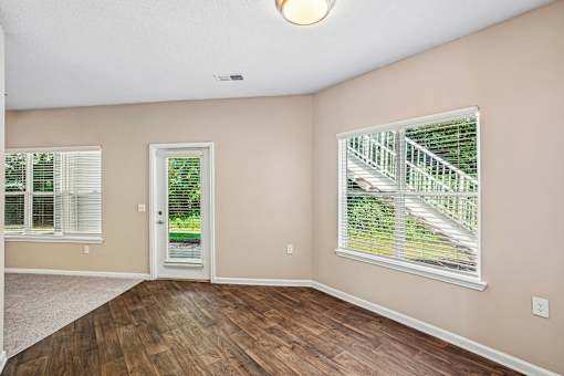 A room with a wooden floor and a window with a view of a staircase.