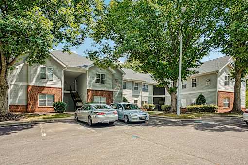 Two cars are parked in front of a building with a tree in front of it.