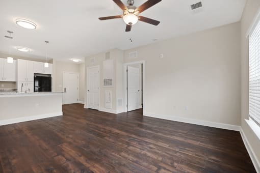 an empty living room with a ceiling fan and a kitchen