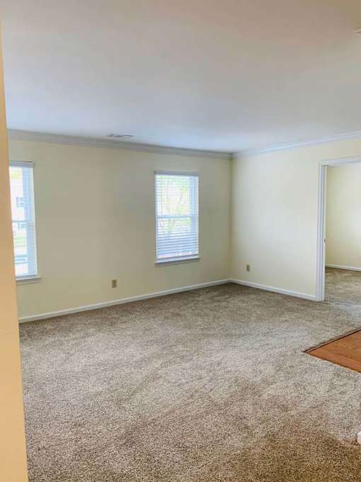 A room with a carpeted floor and two windows.