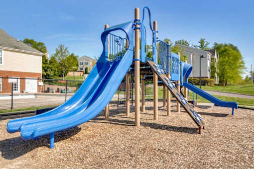 A blue slide in a playground with a wooden structure.
