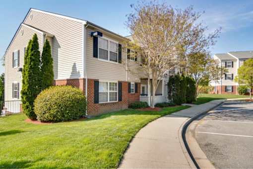 A residential building with a white and beige exterior and a green lawn in front.