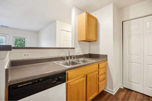 A kitchen with a black dishwasher and wooden cabinets.