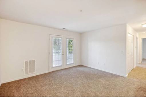 A room with a carpeted floor and a window with a view of trees.