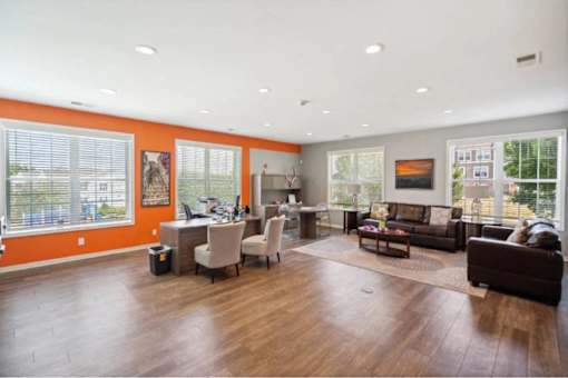 A spacious living room with a brown leather couch and a wooden floor.