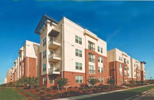 A large apartment building with multiple balconies and a green lawn in front.