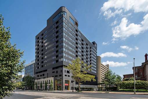 A large modern building with a lot of windows is surrounded by trees and other buildings.