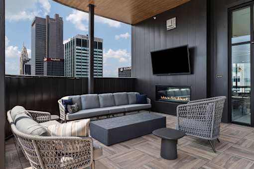 A modern balcony with a grey sofa, wicker chair, and a television.