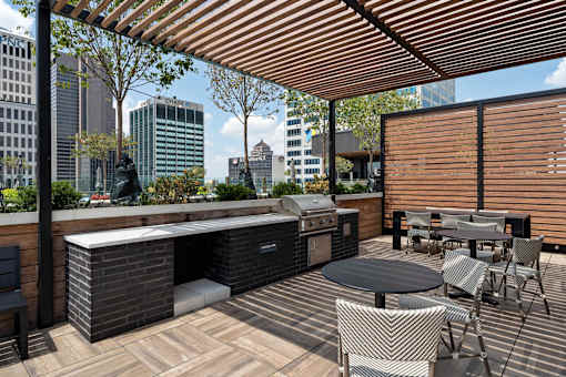 A patio with a grill and chairs overlooking a city skyline.