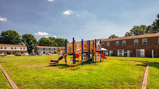 A playground with a swing set and a red slide in the foreground and apartment buildings in the background.