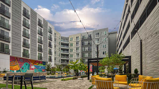 A modern courtyard with a mural, seating, and trees.