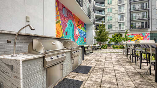 A patio with a grill and chairs is surrounded by a colorful mural.