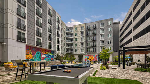 A pool table is in the middle of a grassy area surrounded by buildings.